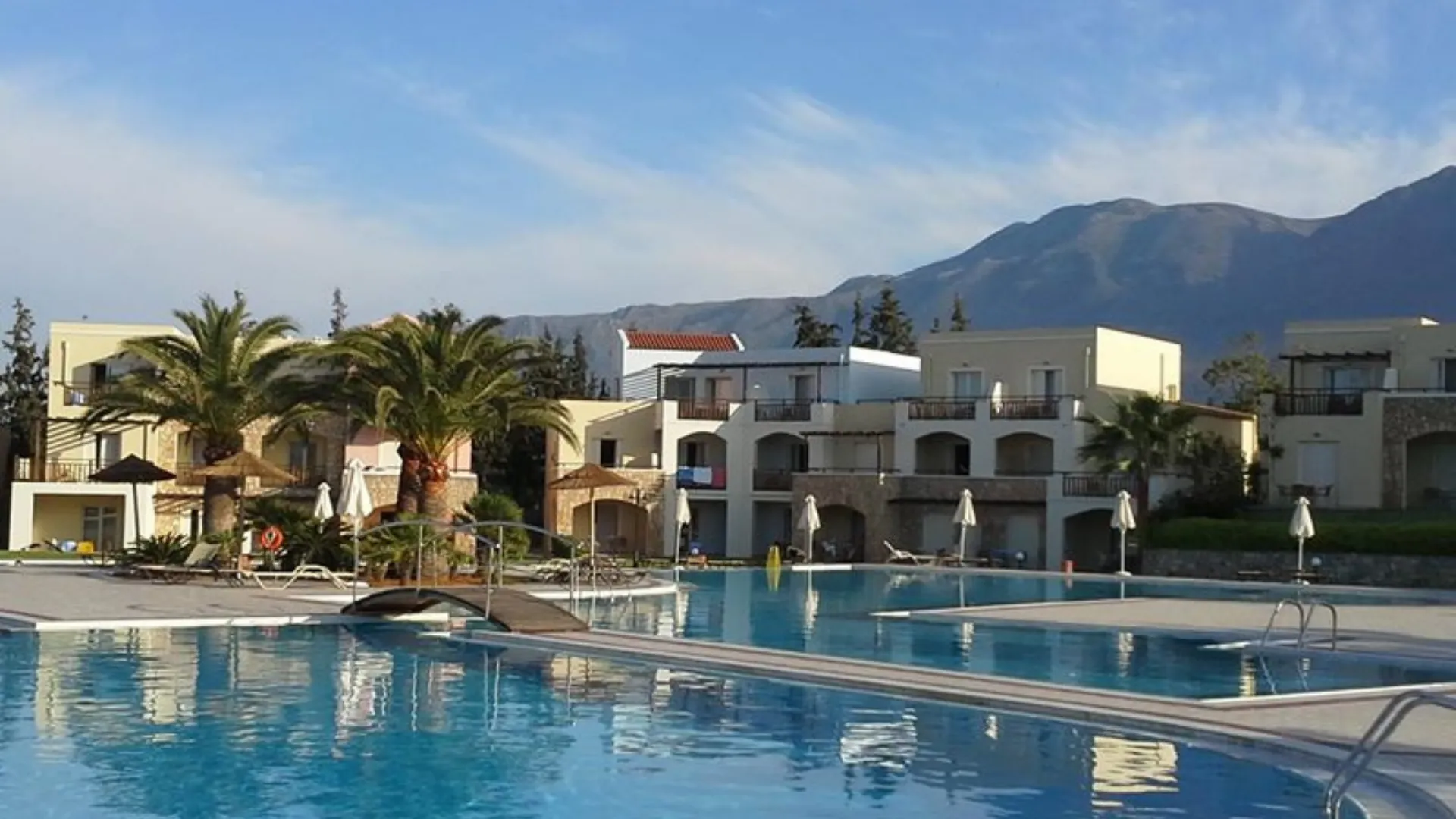 “Sunlit serenity in Elounda - palm trees, cool blue water, and the mountains standing guard over a perfect Cretan afternoon.”